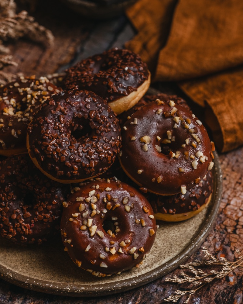 Czekoladowe donuty z posypką na rustykalnym talerzu - fotografia deserów